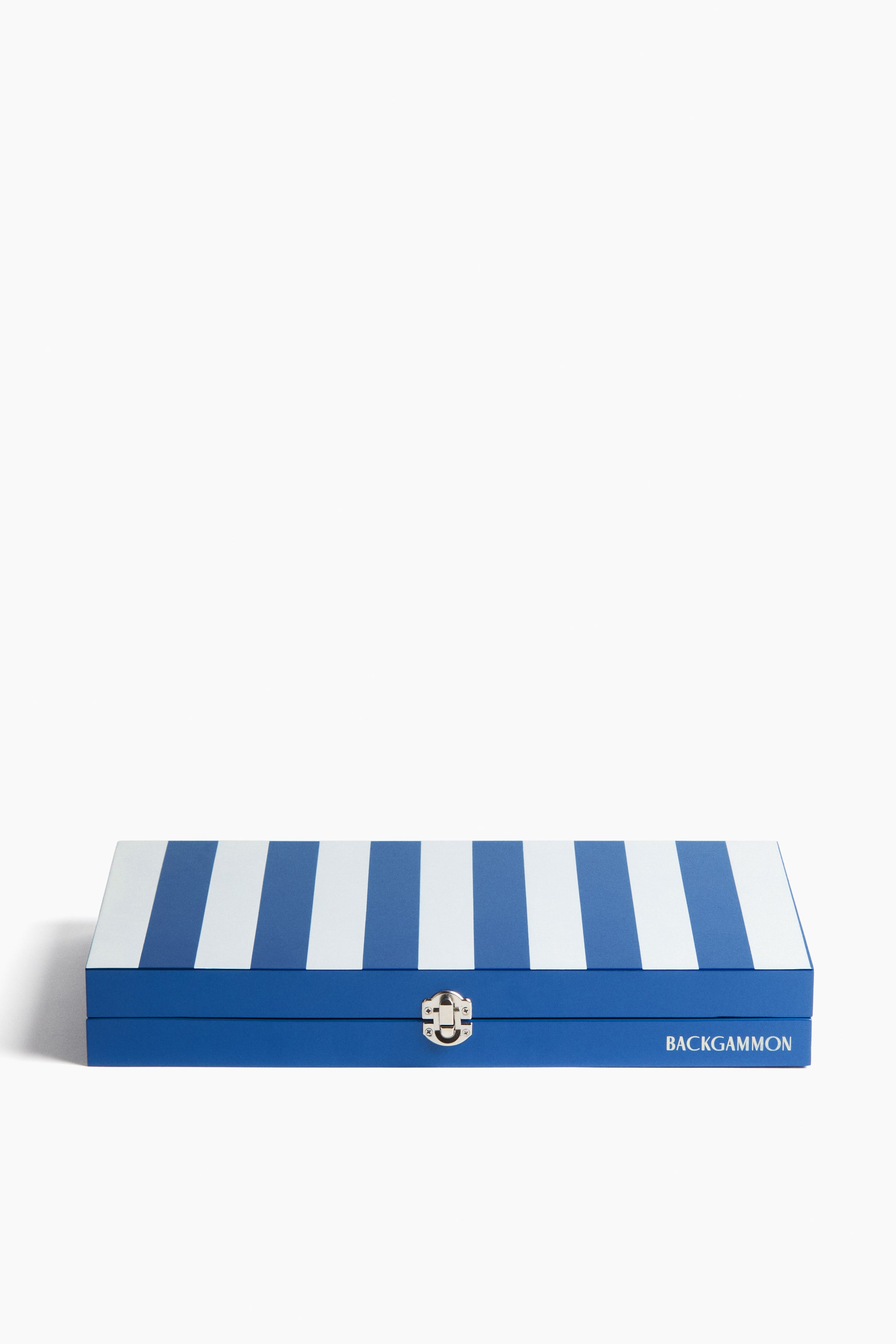 View larger image: The backgammon set box showcases alternating blue and white vertical stripes on its top surface. The solid blue front features a centrally positioned silver-coloured clasp, with the word "BACKGAMMON" printed in white on the right.