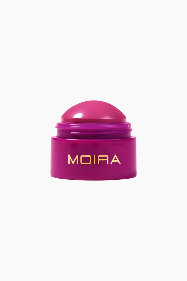 En magenta krukke med kosmetisk produkt vises forfra, med merkenavnet "MOIRA" i gullbokstaver, og et glansfullt, kuppelformet, intensivt rosa produkt som hever seg fra midten. - 1
