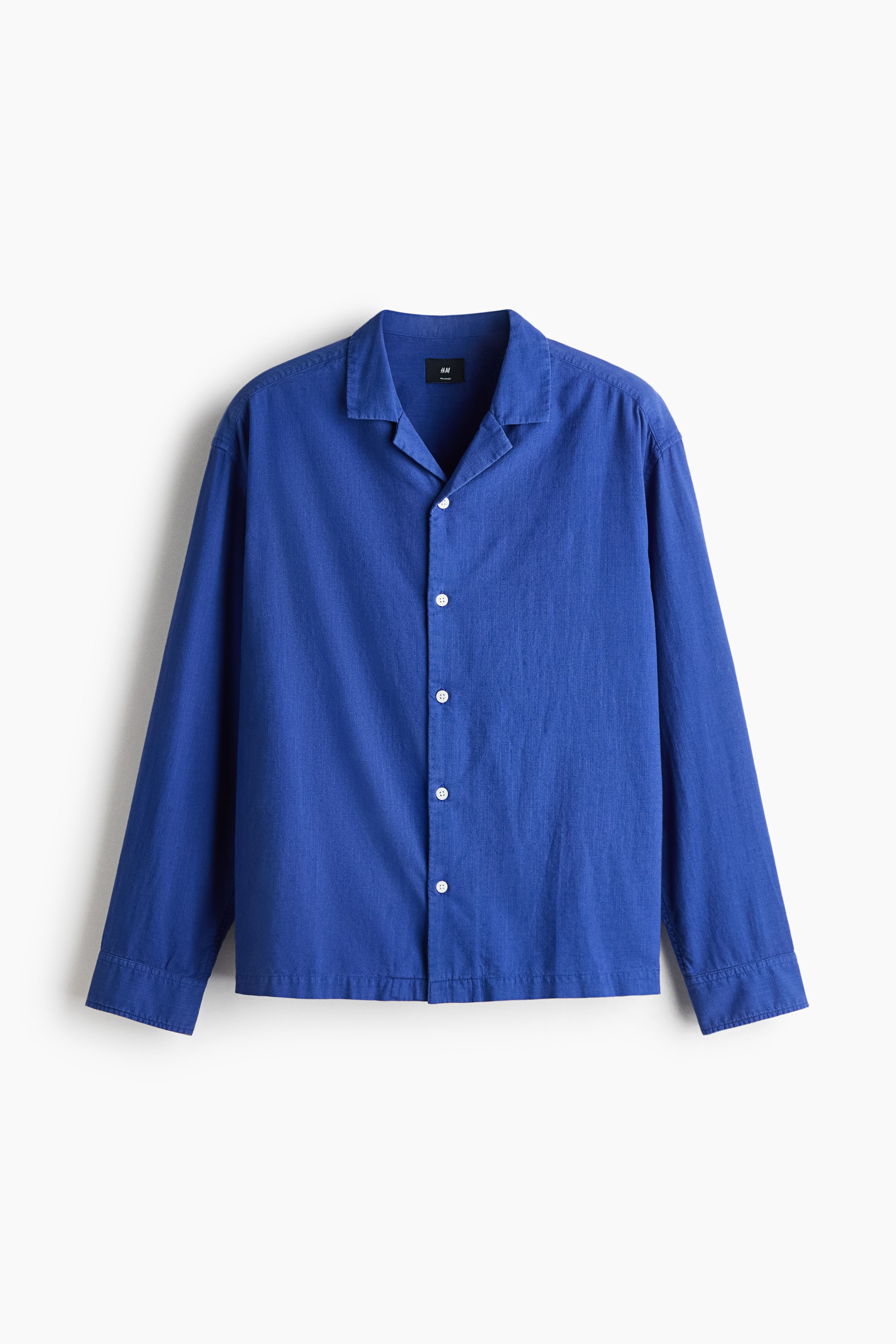 View larger image: A bright blue long-sleeve cotton shirt is hanging flat and facing forward, showcasing its relaxed fit. It features an open resort collar, a French front with five white buttons, and long sleeves with buttoned cuffs.
