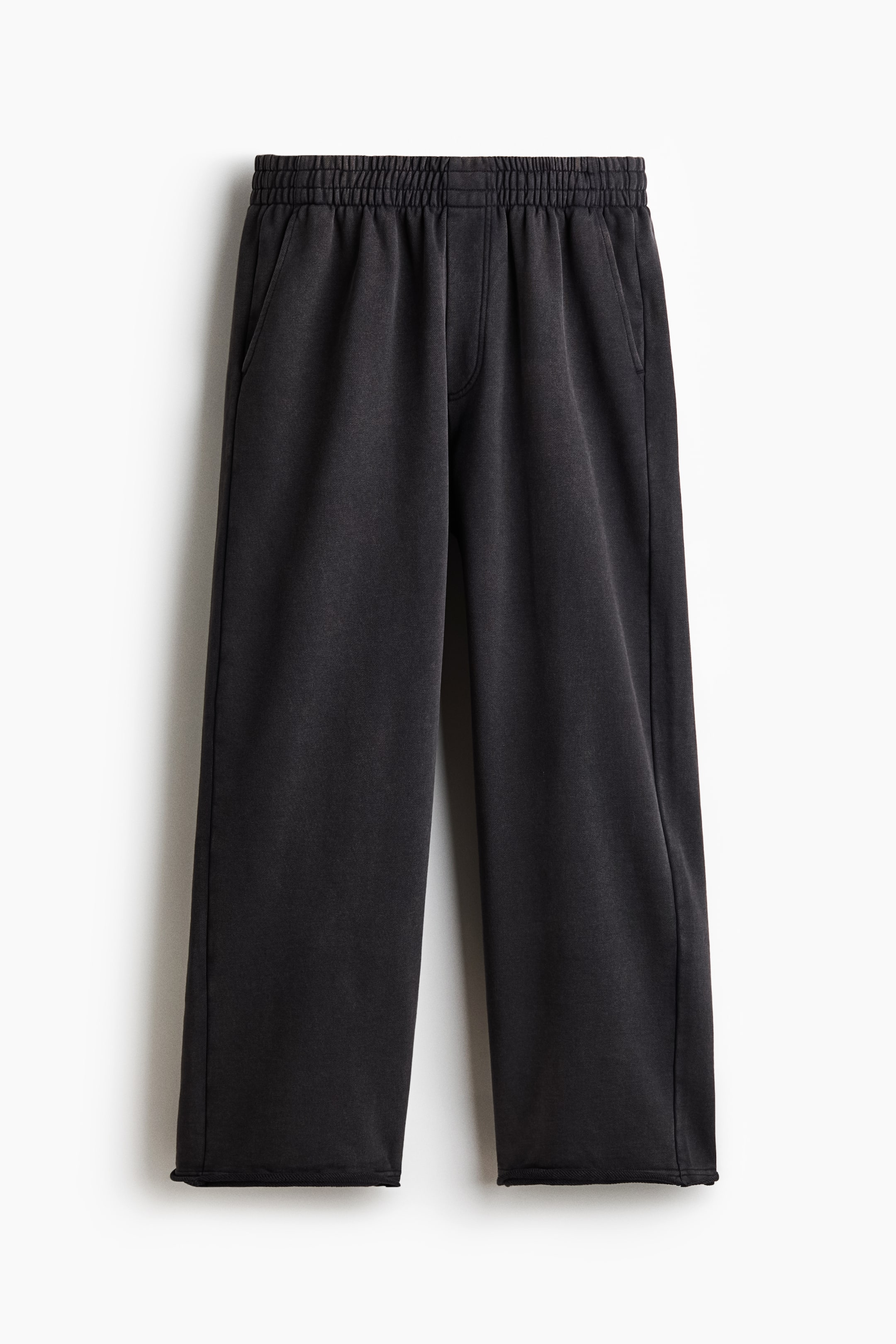 View larger image: Washed black wide-leg sweatpants are shown from the front, featuring an elastic waistband, two side pockets, and raw-edge hems.