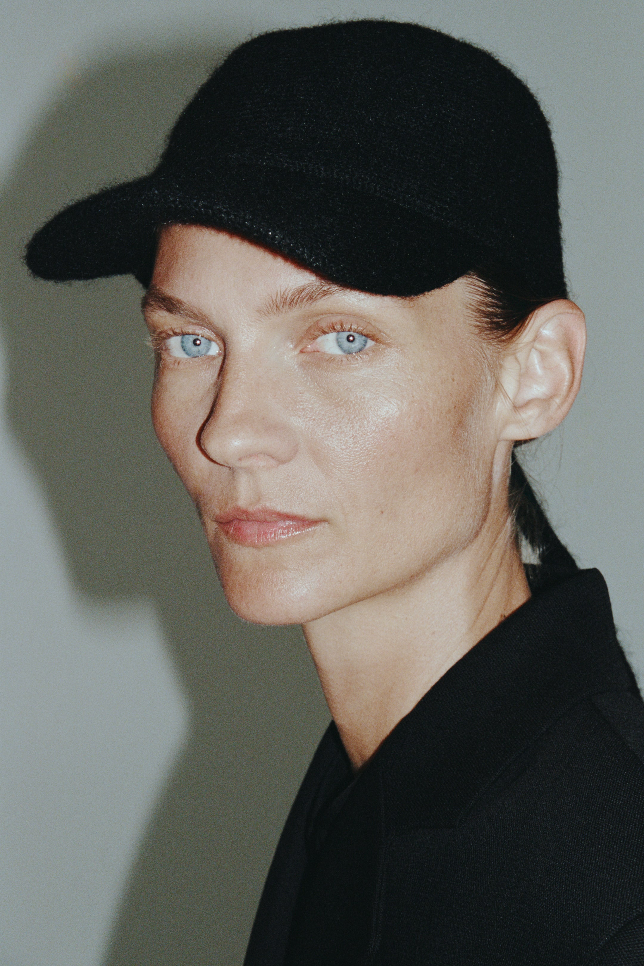 View larger image: A black knitted cap featuring a soft, textured finish and a curved brim is being worn by the model. The cap is styled alongside a matching black collared garment.