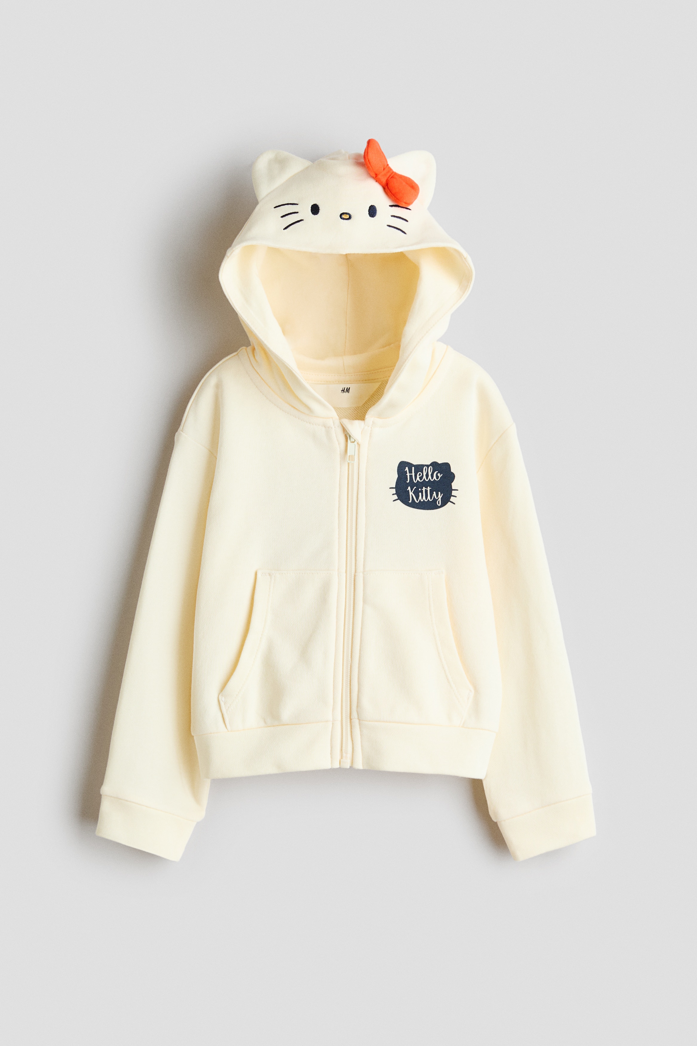 ã¯ãªã¼ã è²ã®ã¸ããã¢ãããã¼ãã£ã¼ãçç¨ããã¢ãã«ããè¸å
ã«å°ããªHello Kittyã®ã°ã©ãã£ãã¯ãæ½ãããã¢ã¤ãã ã身ã«çãã両æãããã³ããã±ããã«å
¥ãã¦ç«ã£ã¦ãã¾ãããã¼ãã£ã¼ã¯ãå°ããªã·ã«ãã¼ã®æã§è£
飾ãããç½ããã¥ã¼ã«ã¹ã«ã¼ãã¨åããã¦ã³ã¼ãã£ãã¼ãããã¦ãã¾ãã