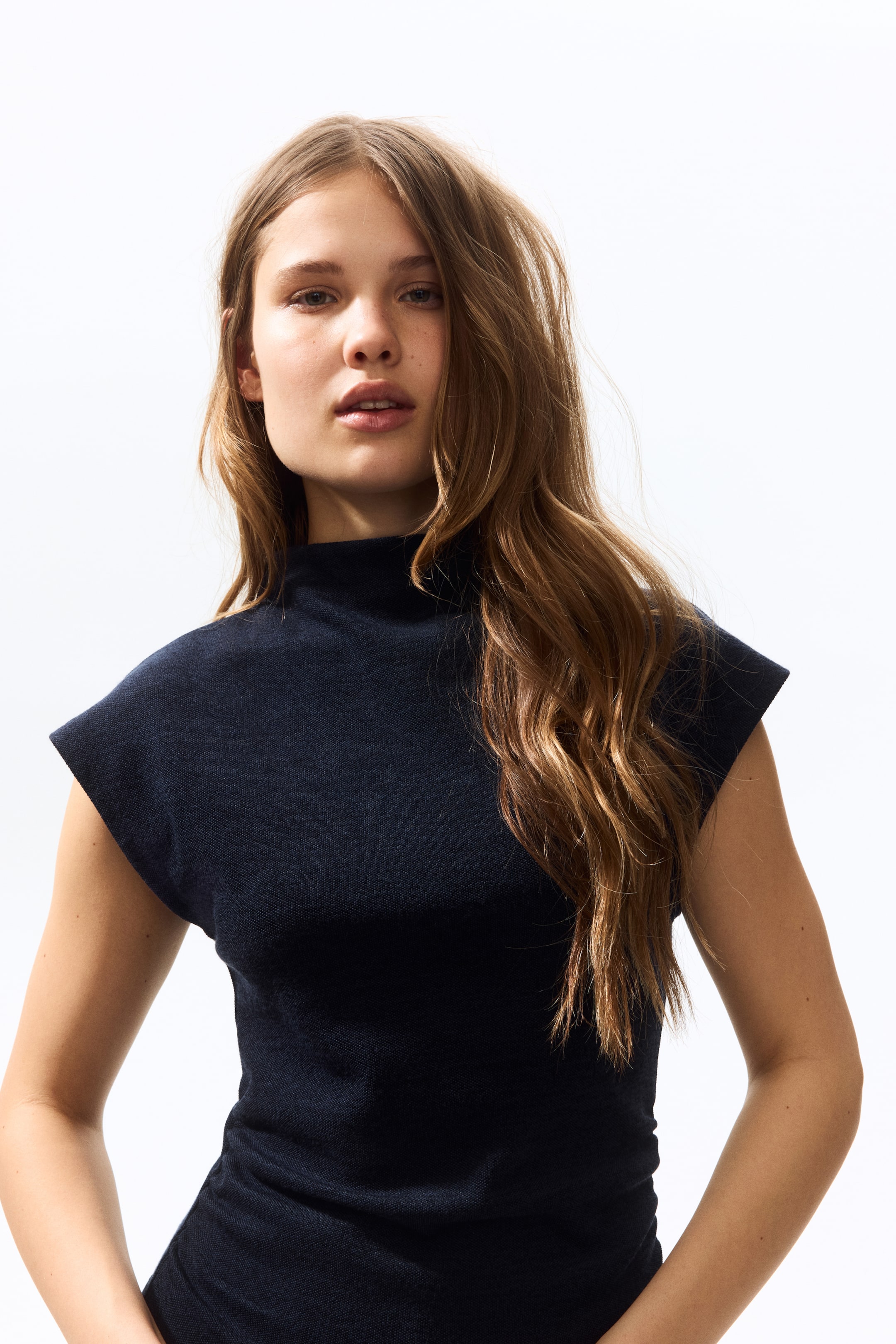 Visualizza immagine più grande: Un top in maglia fine di colore blu scuro con collo alto e maniche corte a cappuccio, che presenta una silhouette aderente.