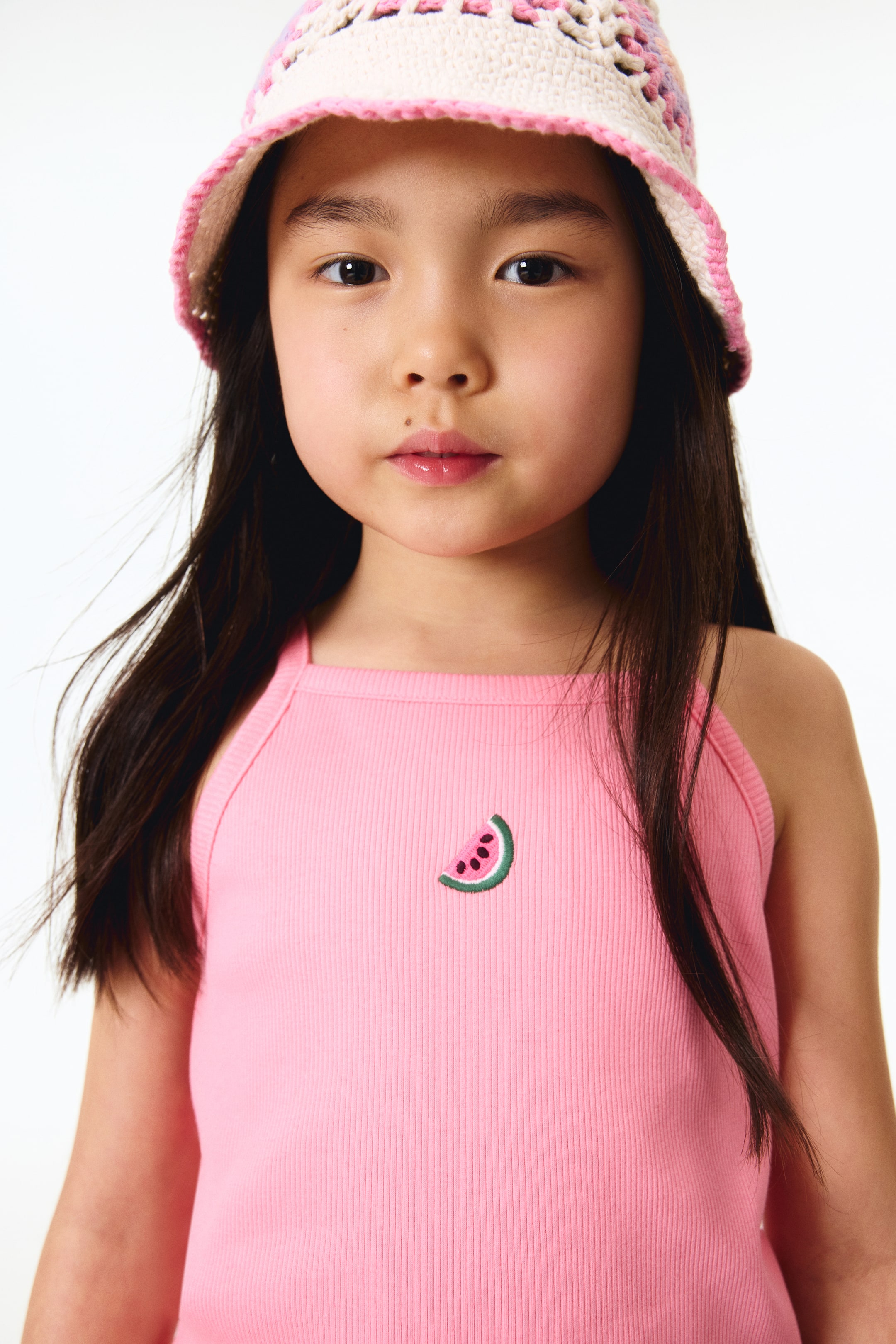 View larger image: A pink ribbed tank top with thin straps is being worn, showcasing an embroidered watermelon slice on the chest that illustrates pink flesh, dark seeds, and a green rind.