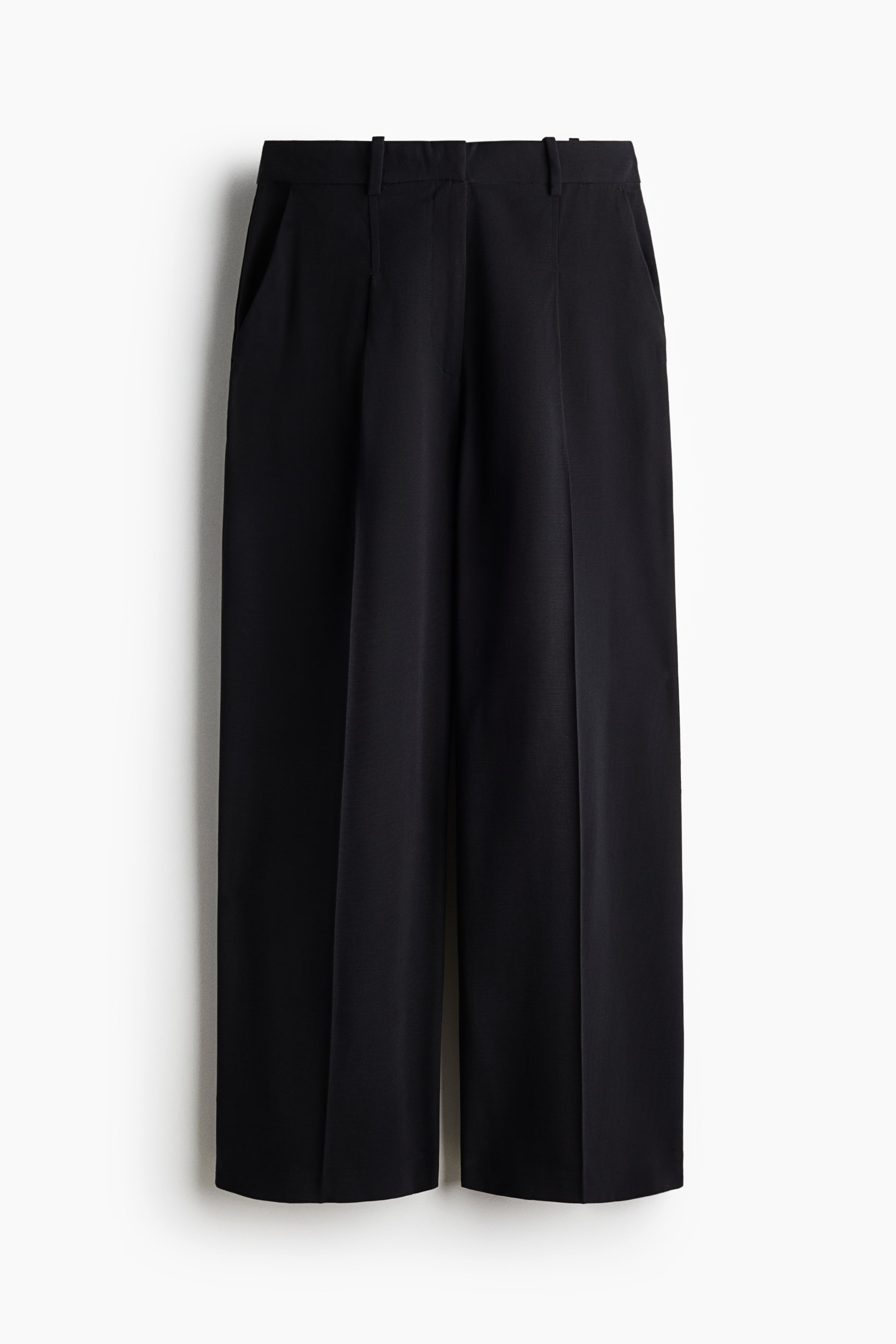 View larger image: Black wide-leg trousers are hanging facing front, featuring a structured waistband with belt loops and front pleats. The trousers are showcasing pressed creases running down the centre of each leg and slanted side pockets.