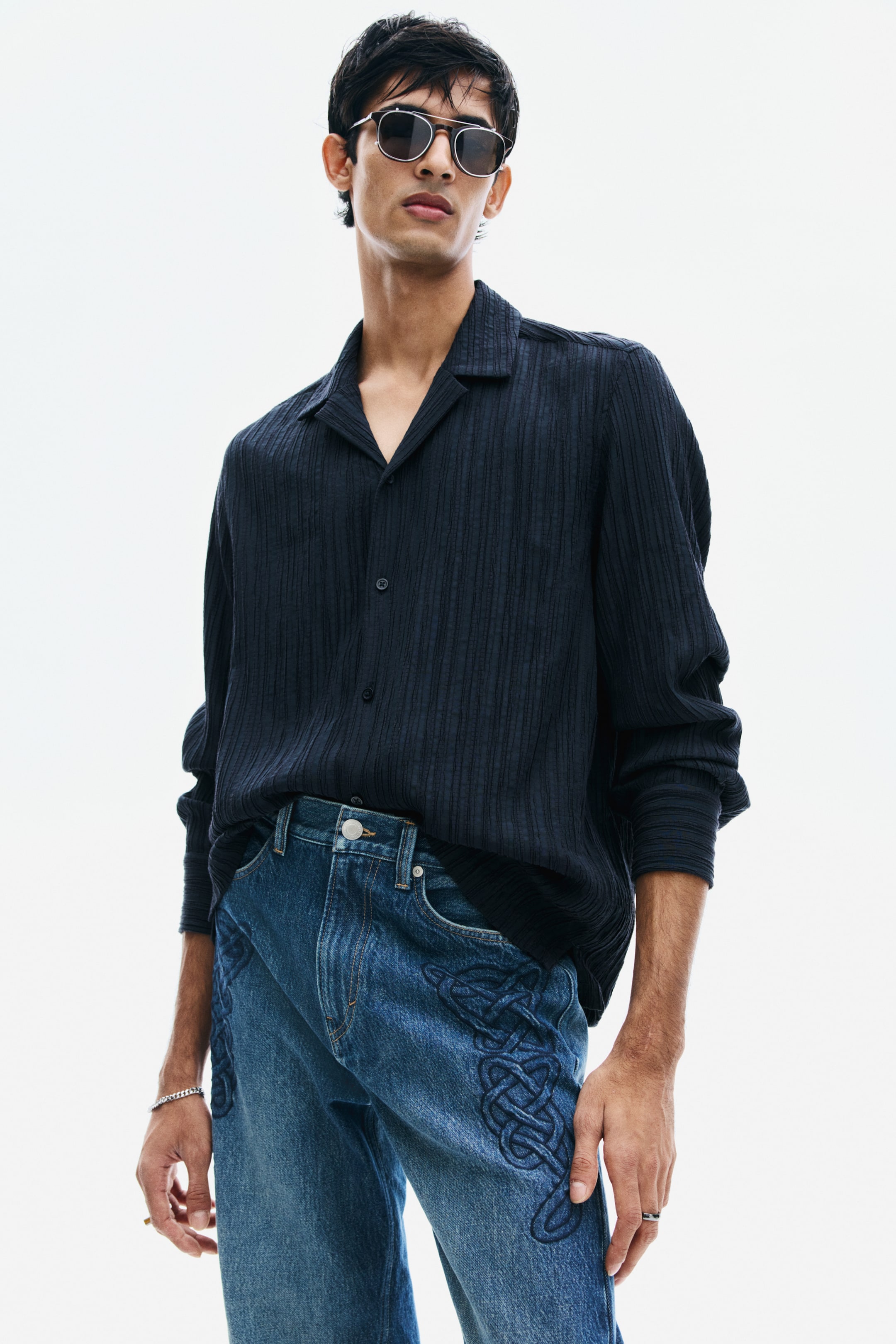 View larger image: A dark navy, long-sleeved shirt in a textured crinkle weave is being worn by the model, with the front loosely tucked into blue jeans. The relaxed-fit shirt features a resort collar and a button-front closure.