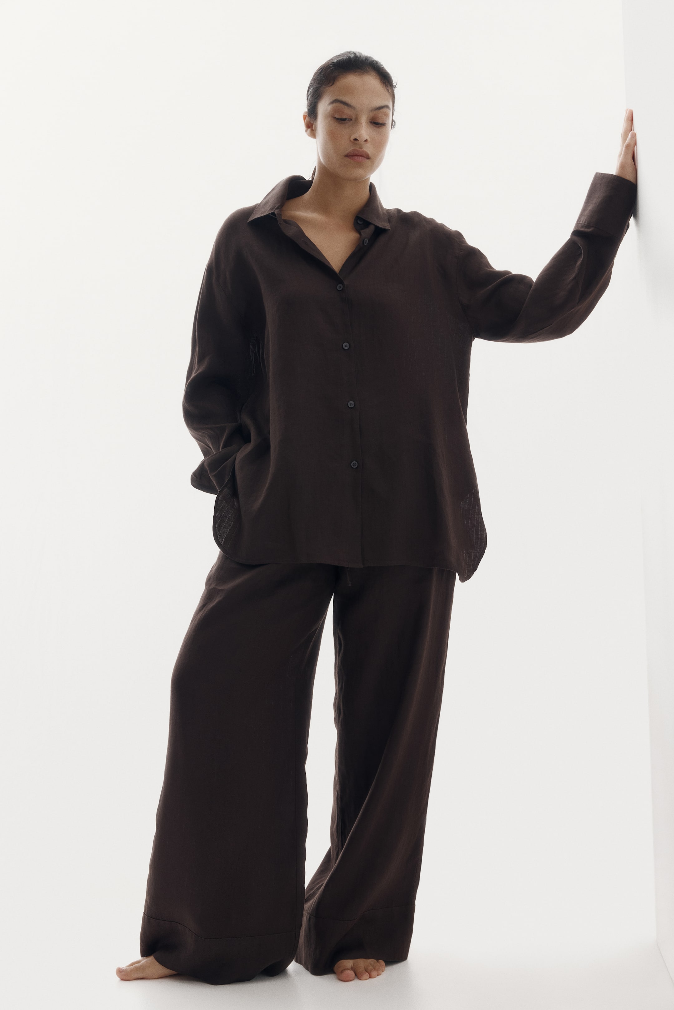 View larger image: A dark brown two-piece set featuring a relaxed fit button-up shirt and matching wide-leg trousers. The shirt is designed with a pointed collar, long sleeves with buttoned cuffs, and dark buttons down the front, while the full-length trousers showcase a loose silhouette.