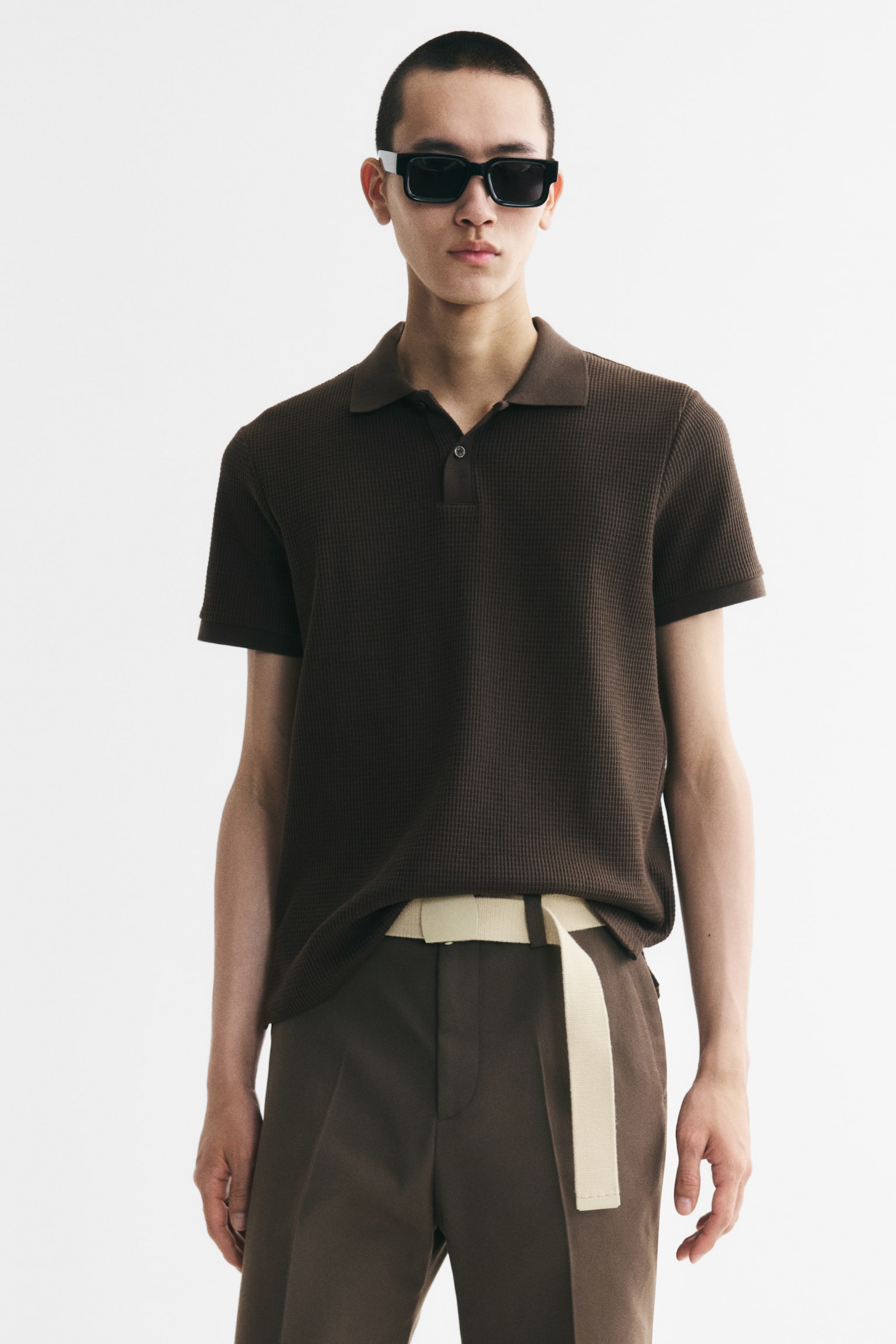 A dark brown polo shirt is showcased from the front, boasting a distinct waffle-knit texture. It is crafted with a collar, a two-button placket, ribbed short sleeves, and a straight hem, indicating a slim fit. - 1