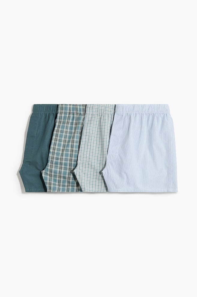 Four pairs of boxer shorts are lying flat, presenting their front upper sections and elasticated waists. One pair is solid teal, two pairs are featuring teal and green plaid designs, and the fourth pair is a light blue with white vertical stripes. - 1