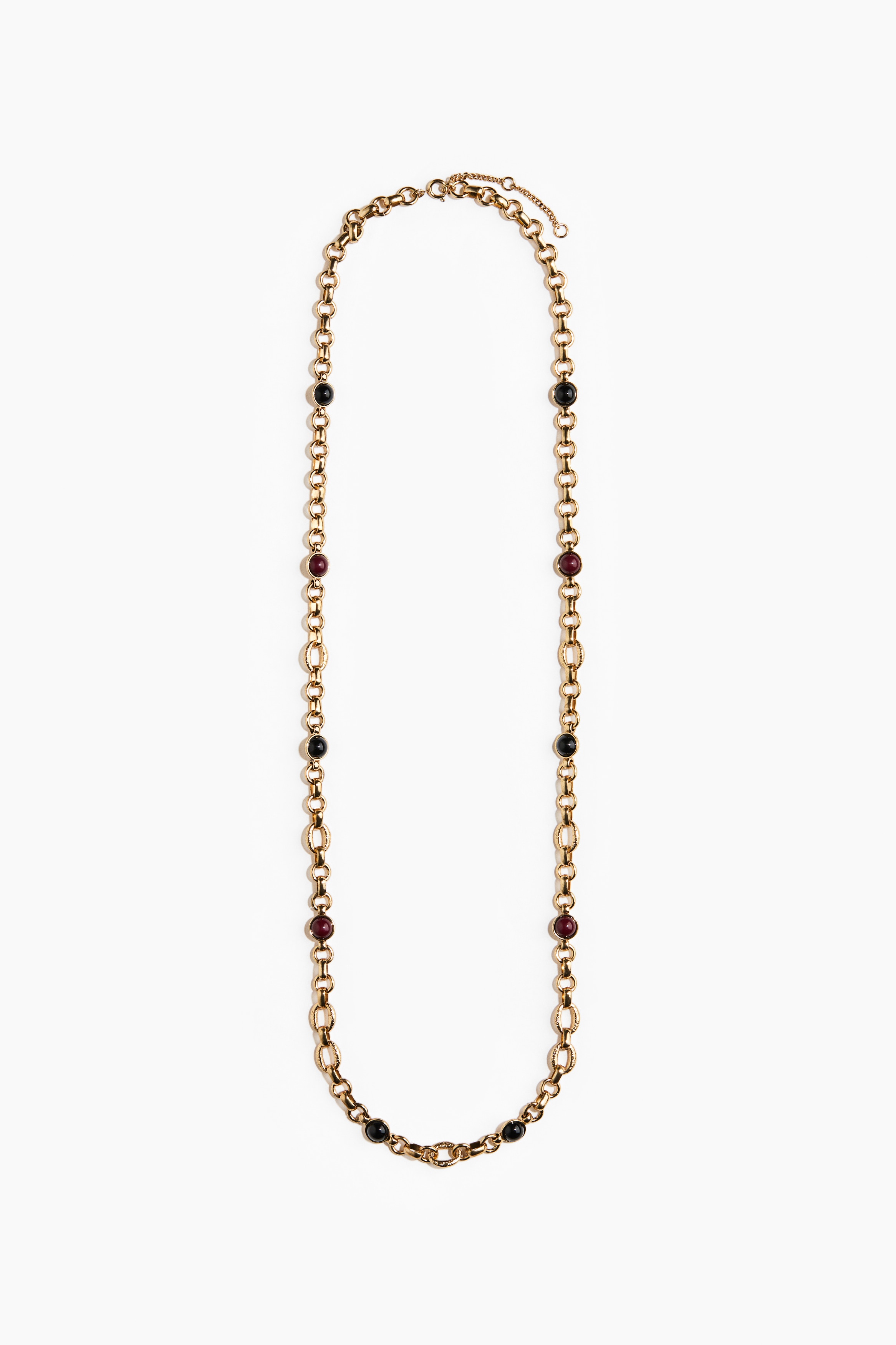 Un collier Ã  chaÃ®nes dorÃ©es superposÃ©es, ornÃ© de petites incrustations de pierre rondes, est portÃ© par le mannequin, associÃ© Ã  de grandes boucles dâoreilles carrÃ©es Ã  texture dorÃ©e avec des centres noirs. Les accessoires sont stylÃ©s avec des lunettes de soleil oversize Ã  monture Ã©caille de tortue, dotÃ©es de verres teintÃ©s jaune, et une veste marron texturÃ©e Ã  motif cachemire.