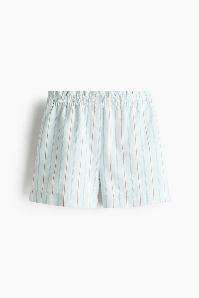 Los pantalones cortos presentan un tejido azul claro con rayas verticales blancas y finas rayas gris oscuro. Cuentan con una cintura elástica fruncida con dos pequeños botones en la parte delantera. - 1