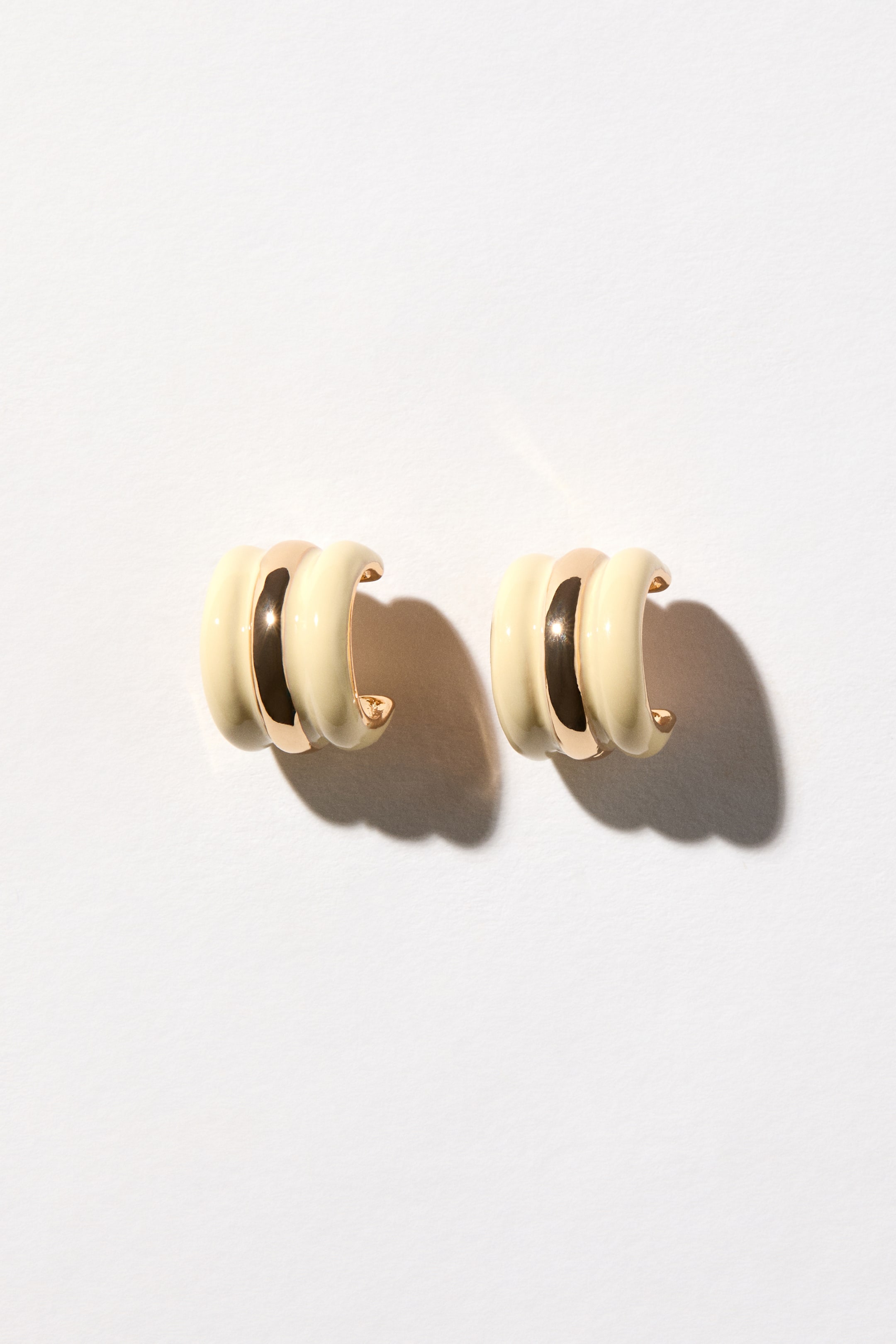 View larger image: Hoop earrings featuring a fluted design with alternating bands of gold-toned metal and cream enamel.