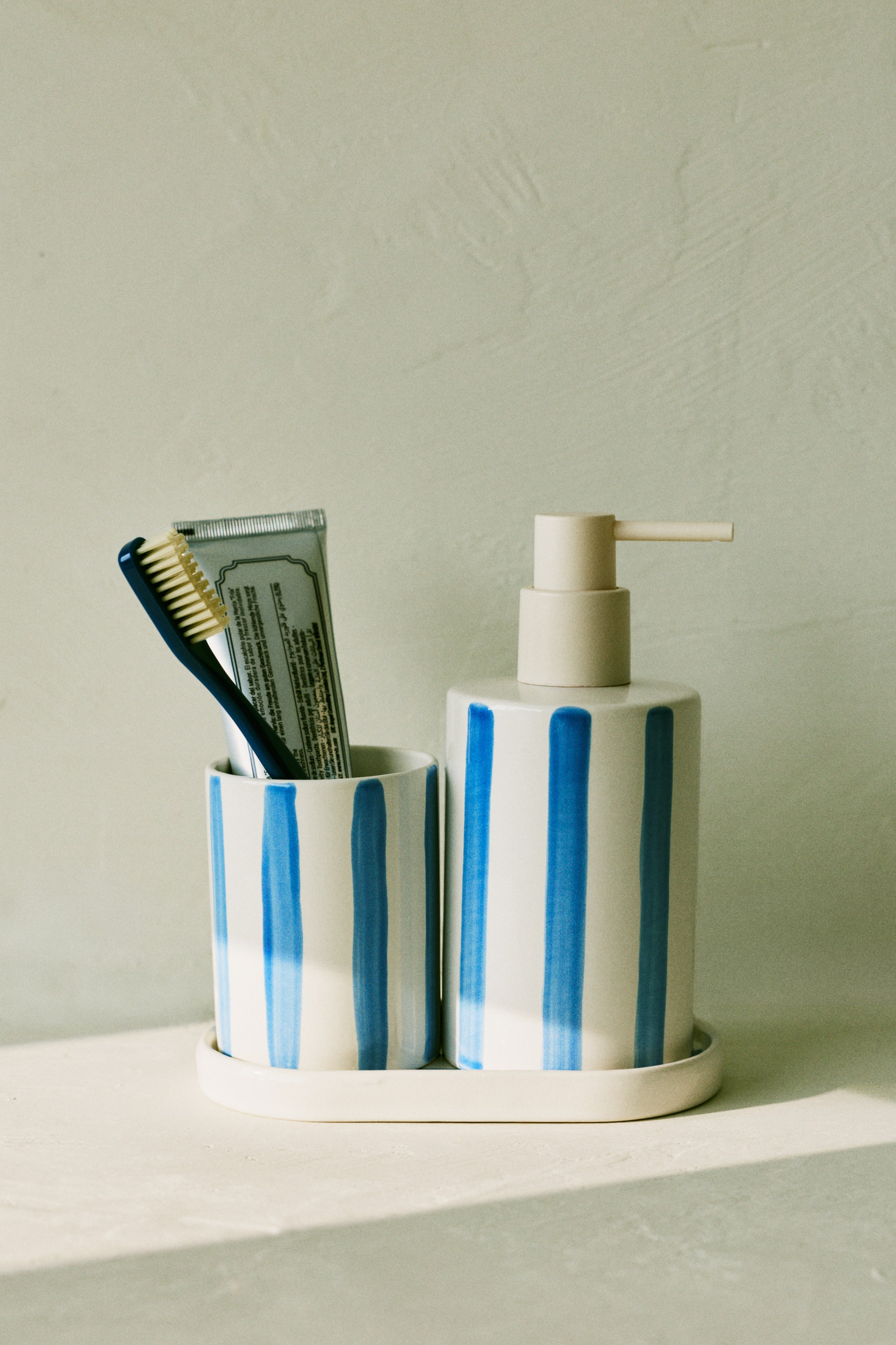 View larger image: "The soap dispenser, crafted from stoneware, showcases a striped design in a front-facing view. It features a cylindrical white body adorned with vertical blue brushstroke stripes, complemented by a light beige pump."
