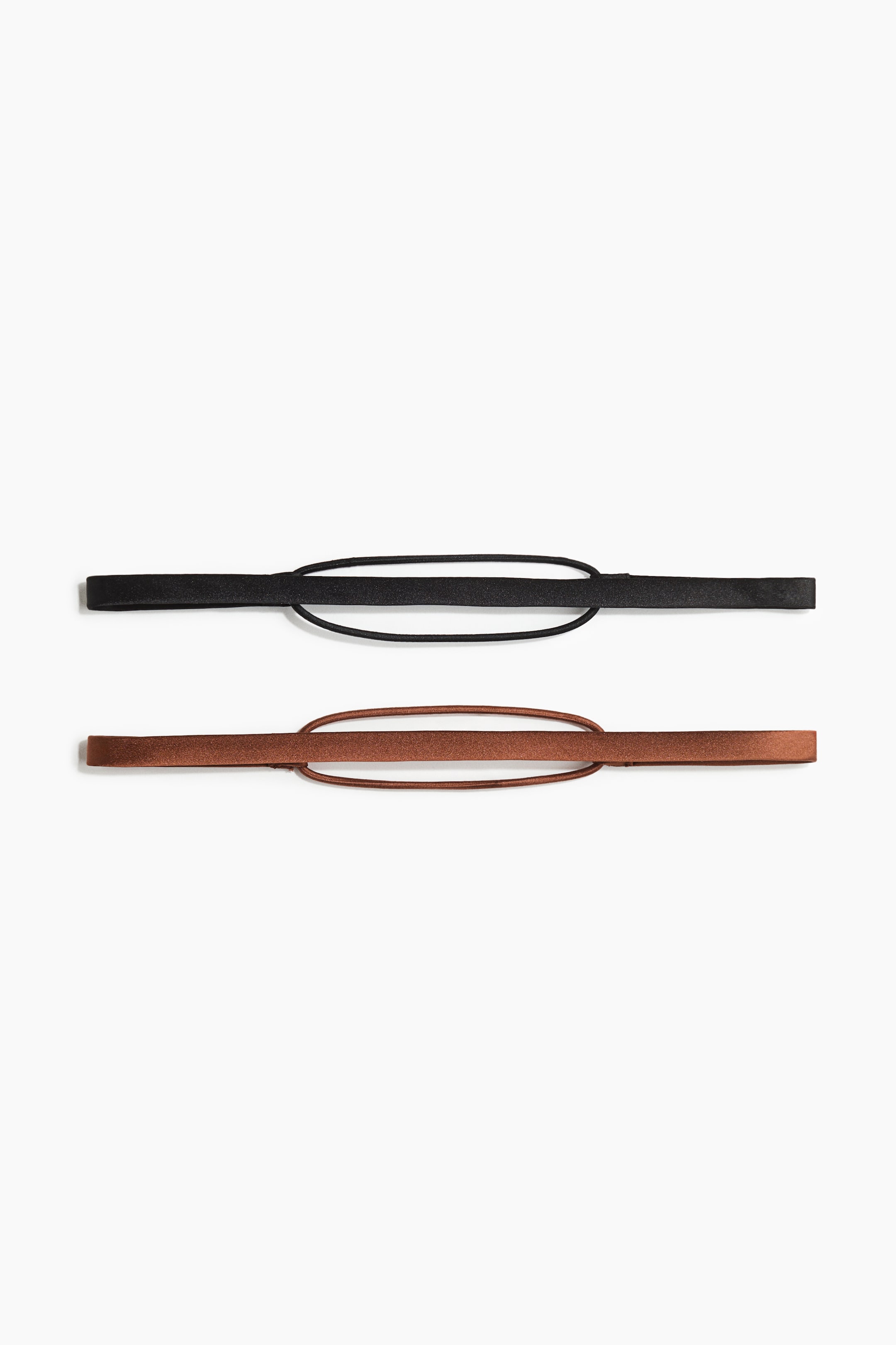 Visa större bild: Ett set med två hårband ligger plant. Det svarta hårbandet och det bronsfärgade hårbandet visar var och en upp ett platt, smalt band som är anslutet till en tunn, elastisk oval ögla.