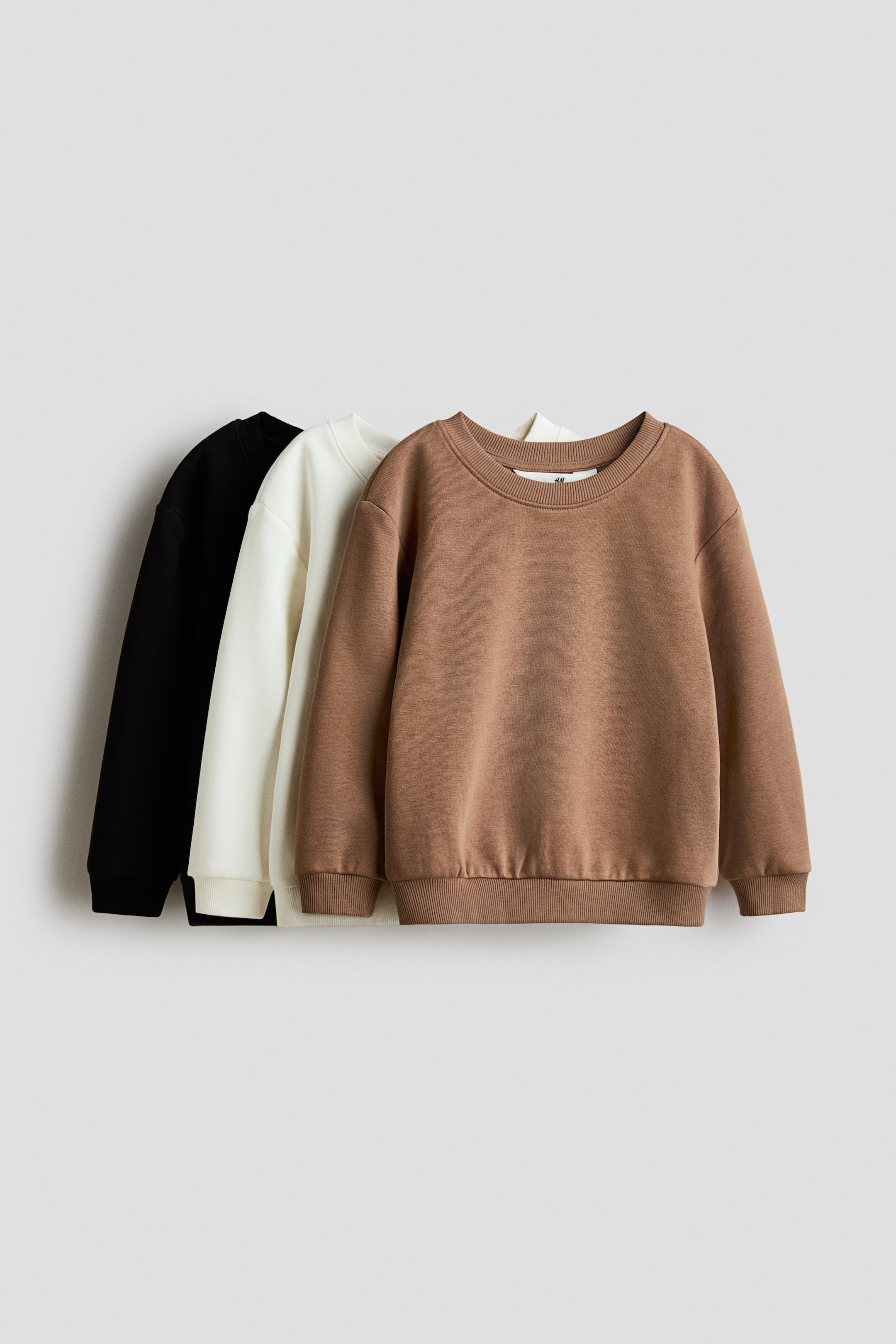 Agrandir l'image: Trois sweatshirts à manches longues sont présentés de face, en noir, blanc cassé et marron. Chaque sweatshirt présente un col rond, des épaules tombantes et des détails côtelés au niveau du col, des poignets et de l'ourlet.