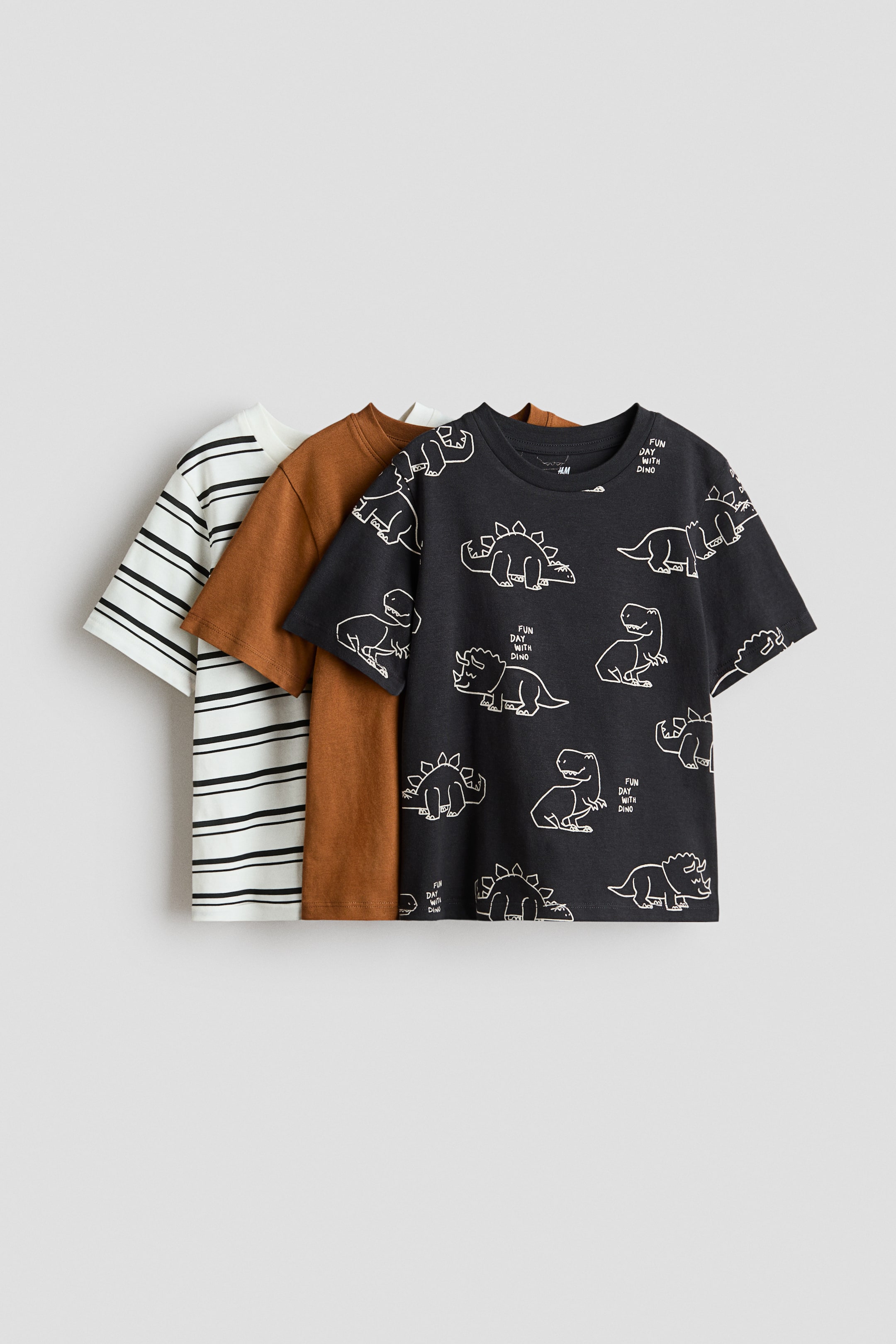 View larger image: Tiga helai t-shirt berlengan pendek disusun, menampilkan pandangan hadapan mereka. T-shirt hadapan berwarna hitam dengan ilustrasi dinosaur berbingkai putih dan teks "fun day with dino", t-shirt tengah berwarna coklat karat solid, dan t-shirt belakang berwarna putih dengan jalur hitam melintang.