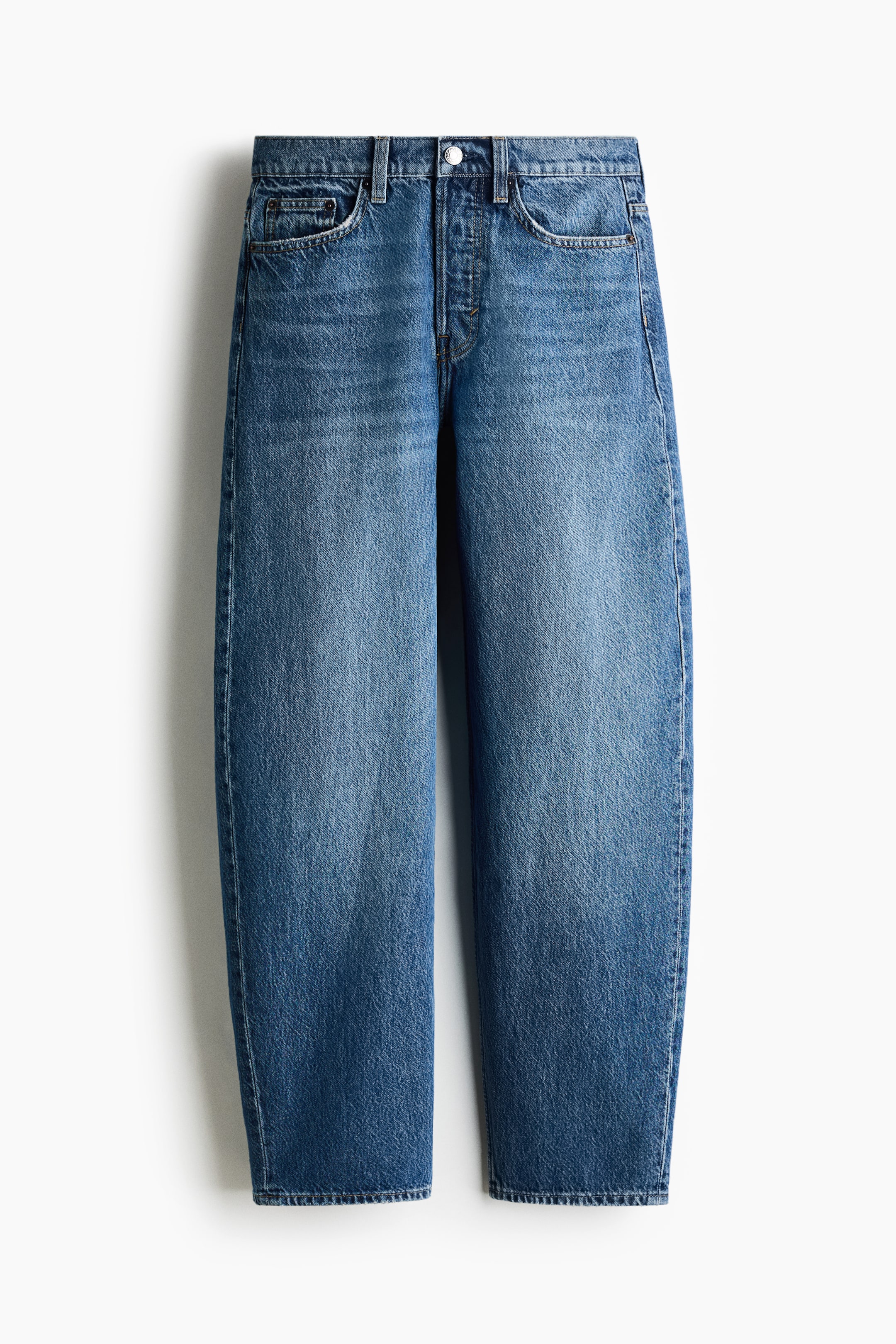 Agrandir l'image: Un jean taille haute à cinq poches, délavage bleu moyen, est présenté de face, avec des jambes courbes et volumineuses qui se resserrent vers l’ourlet. Le jean présente un léger effet délavé et des marques d’usure au niveau des hanches et des cuisses, ainsi que des passants de ceinture et une fermeture à bouton.