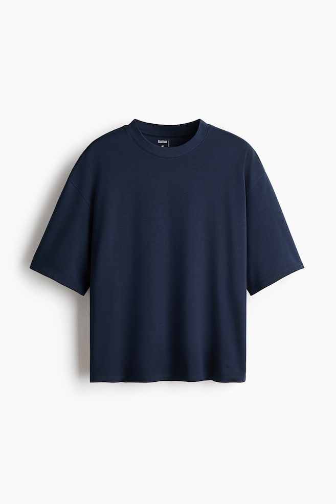 A dark blue t-shirt is presenting from the front, and it is featuring a crew neck and short, wide sleeves. It is having a relaxed, boxy fit with a straight hem, and a small black label is appearing on the inside back neckline. - 1