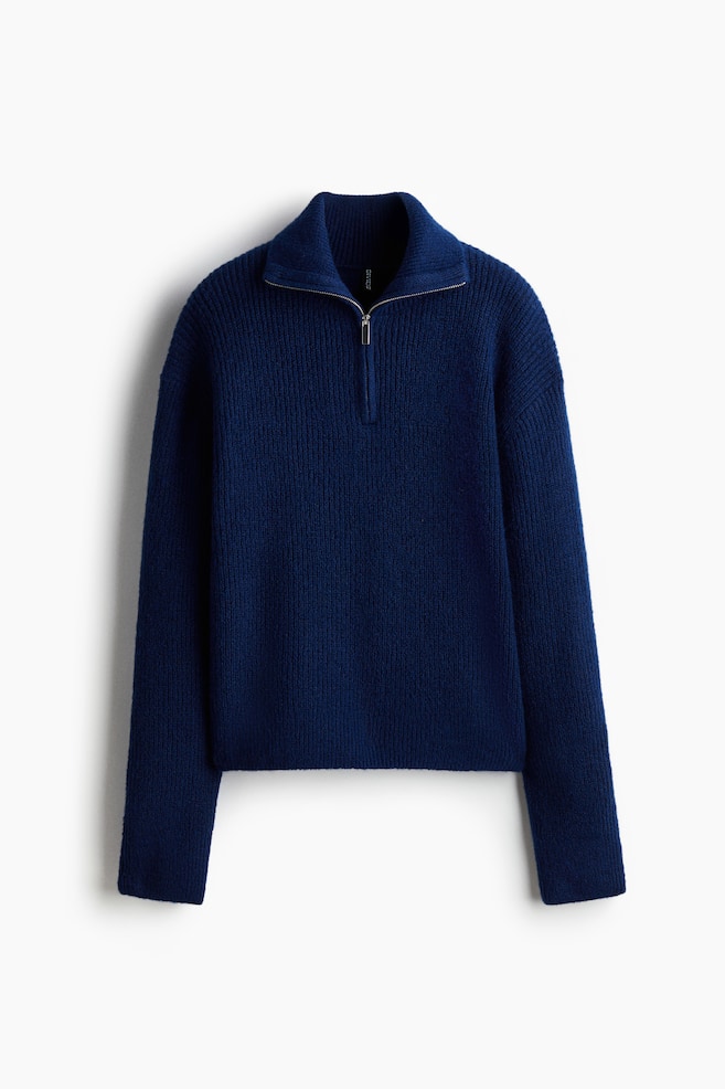 A dark blue quarter-zip sweater is being presented from the front. It is featuring a ribbed knit texture with vertical lines on the body and sleeves, a high stand collar with horizontal ribbing, and a silver-toned half-zip closure. - 1