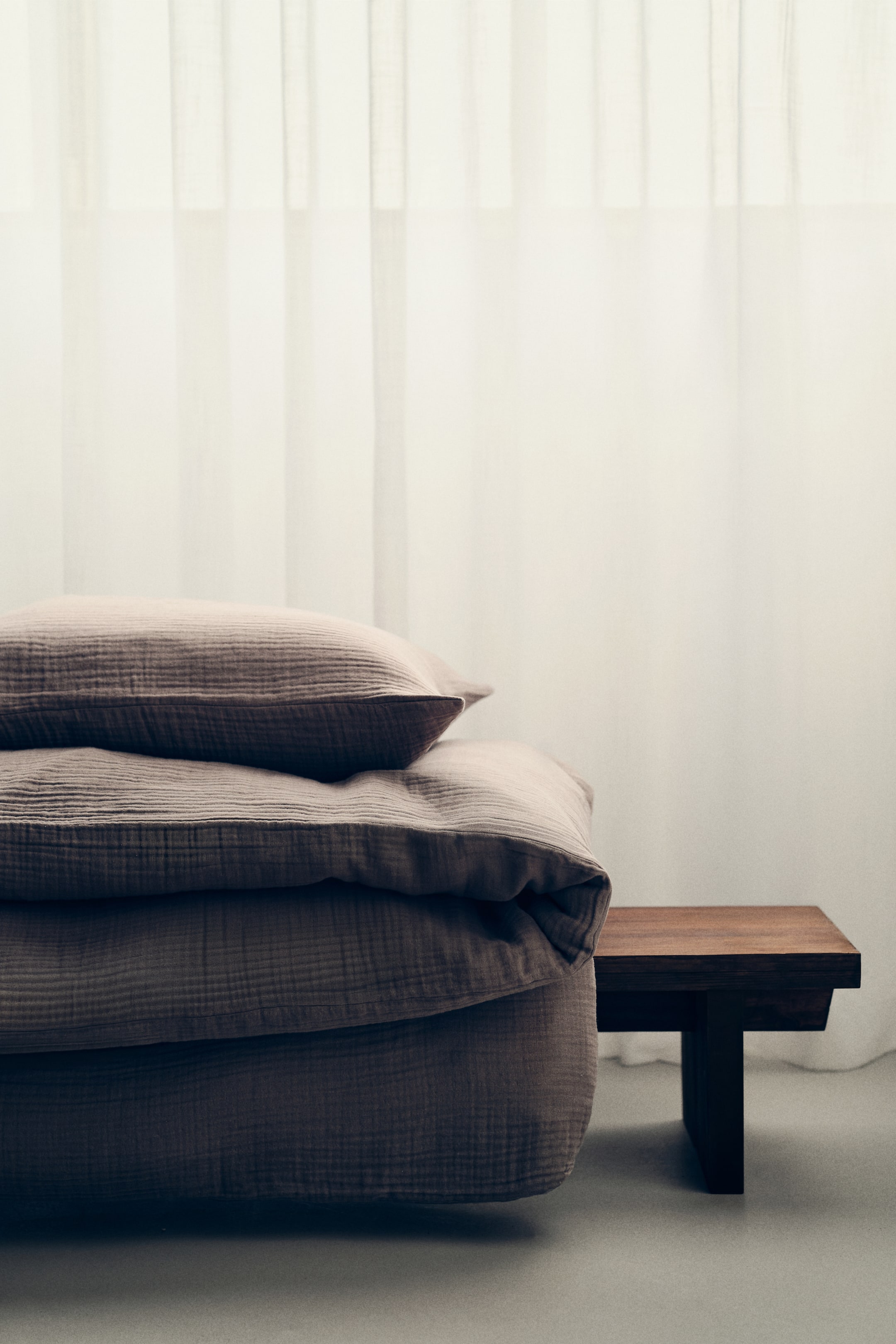 Ampliar la imagen: Un juego de cama en tono topo apagado presenta una almohada esponjosa descansando sobre un edredón doblado, ambos mostrando una textura arrugada distintiva.