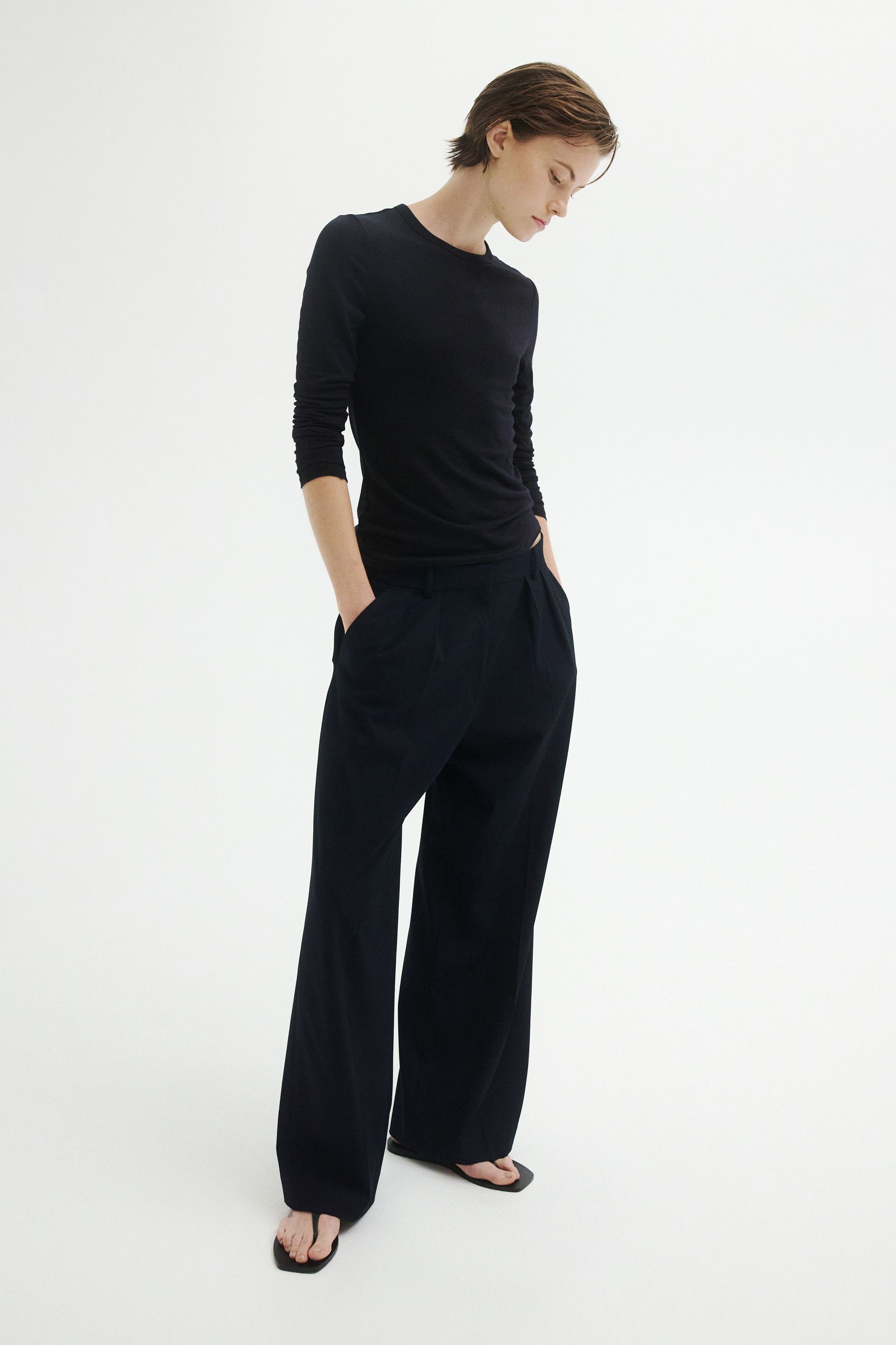 These black wide-leg trousers are hanging front-facing, featuring a structured waistband with belt loops and double pleats. The trousers are draped in a relaxed fit with sharp creases running down the centre of each leg.