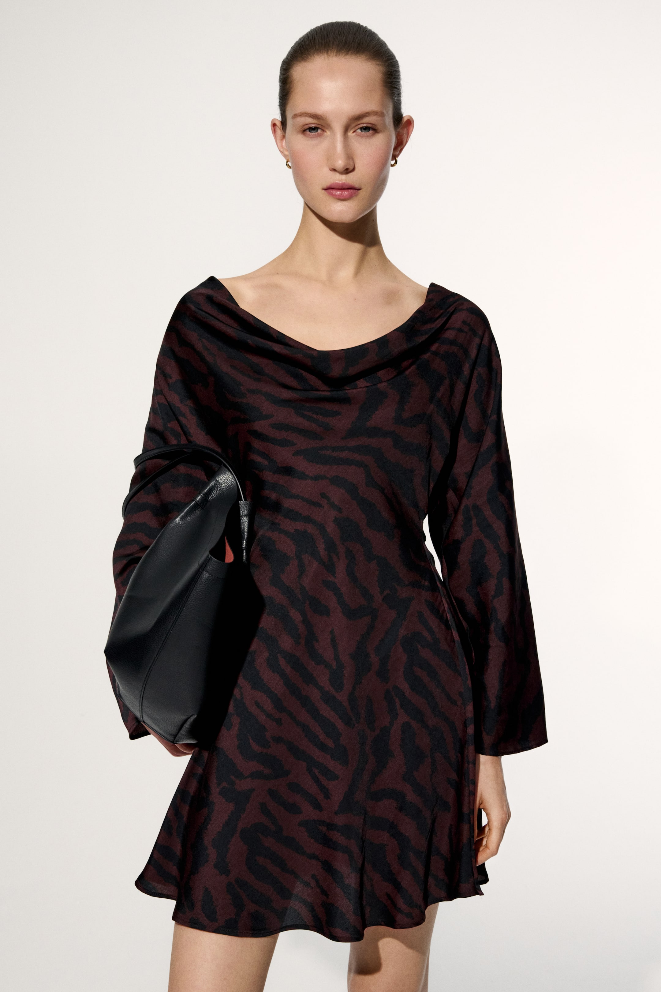 Größeres Bild anzeigen: Ein bordeaux-schwarzes Mini-Kleid mit Zebramuster, das mit einem drapierten Wasserfallausschnitt, langen fließenden Ärmeln und einem sanft ausgestellten Saum versehen ist, wobei eine schwarze Tasche teilweise die linke Seite verdeckt.