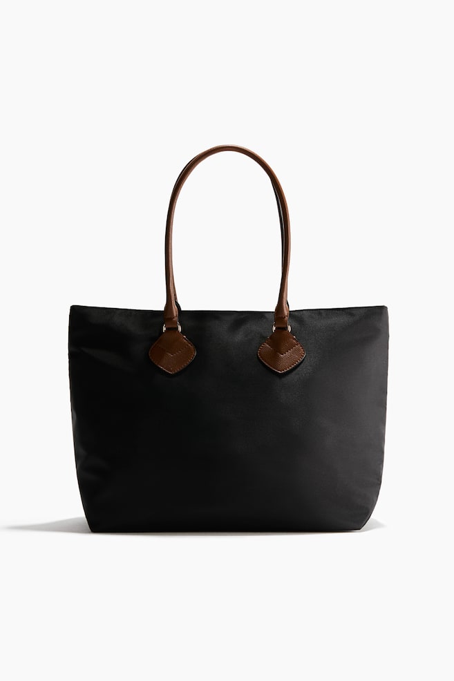 Se muestra de frente un bolso shopper negro de tejido trenzado, con asas tubulares marrones de tejido recubierto sujetas con piezas en forma de rombo. - 1