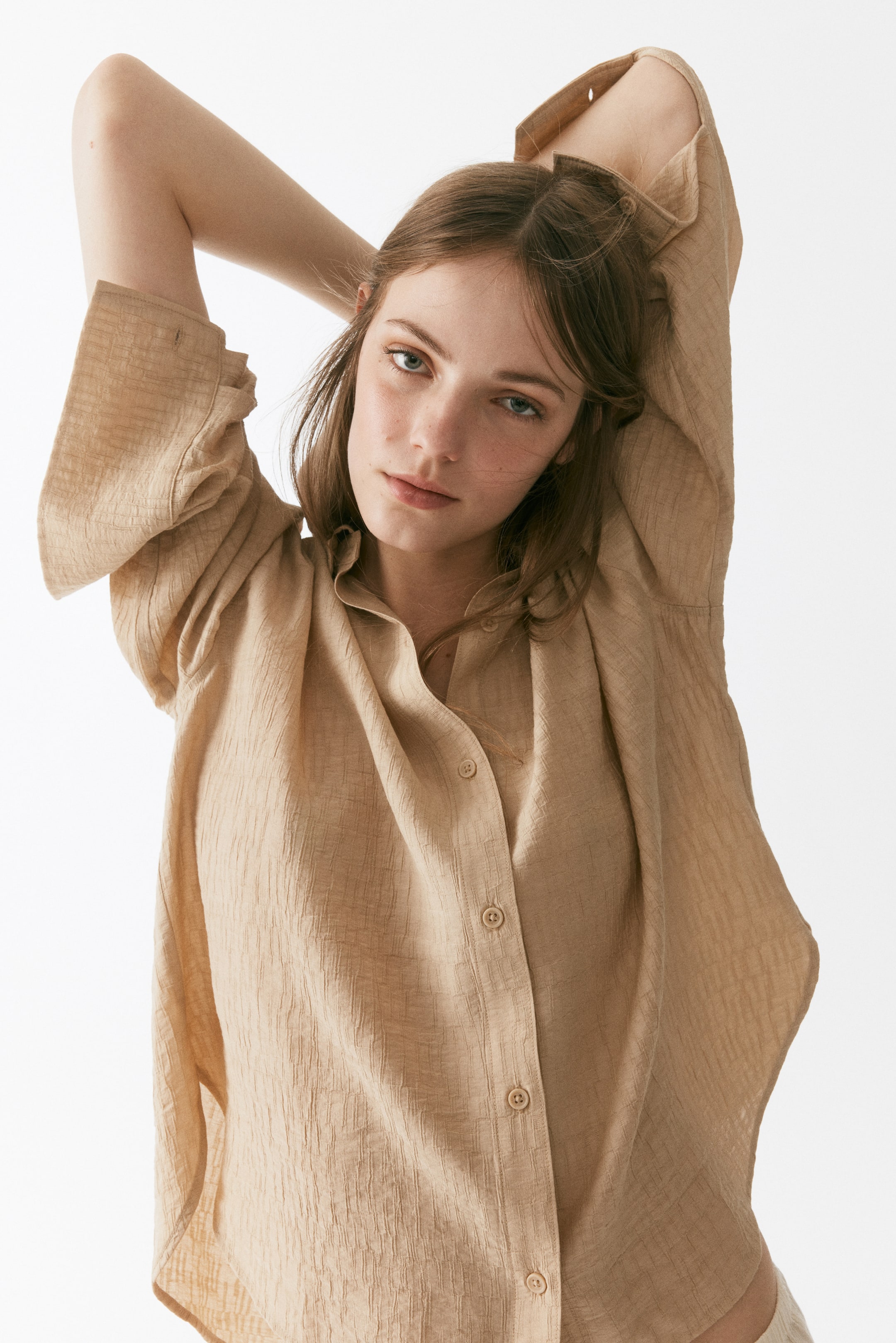 View larger image: Beige shirt with a crinkled texture, featuring a ruffled band collar and a button-down front with matching buttons. Displaying loose, long sleeves with wide, open cuffs.