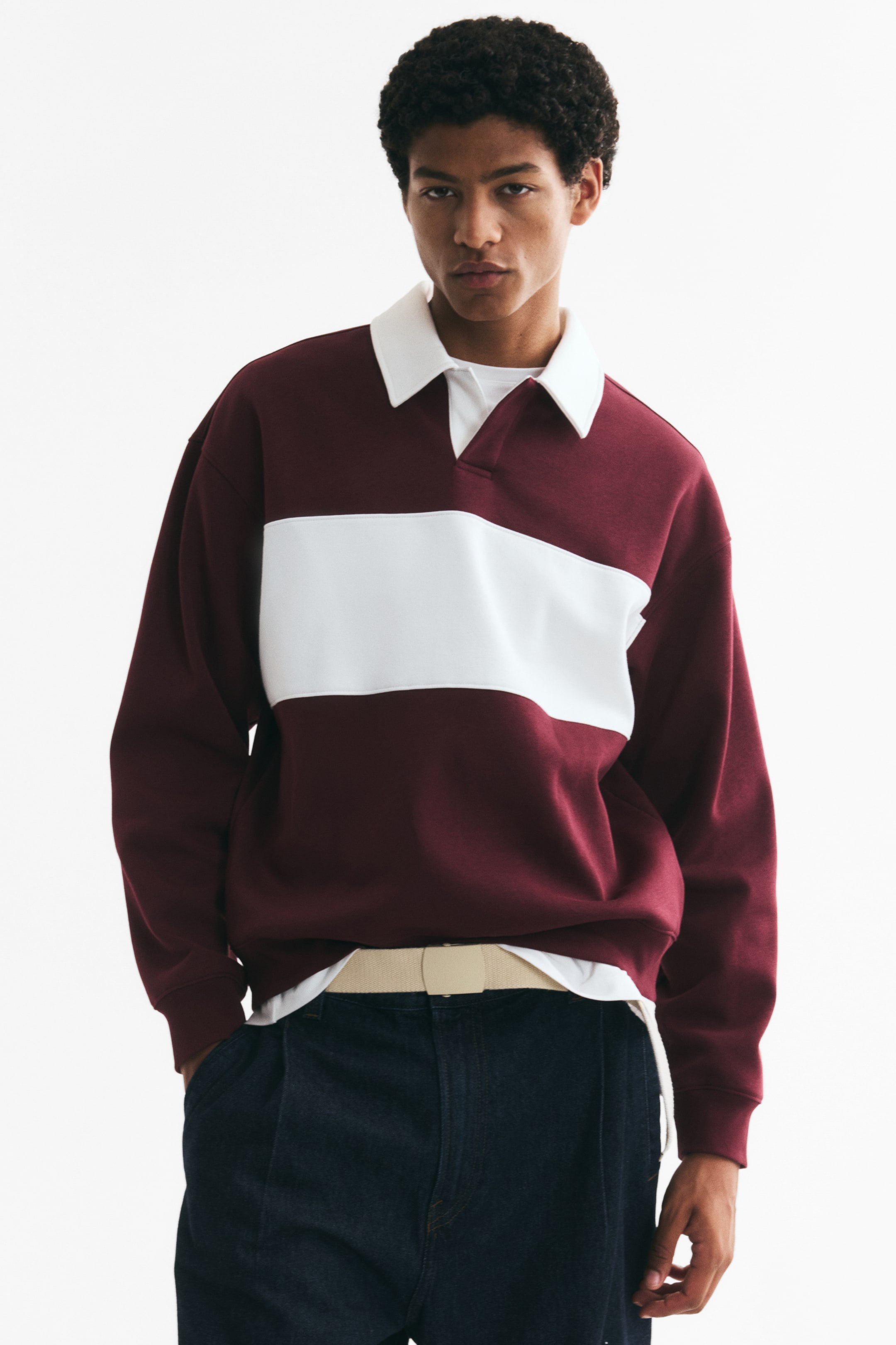 View larger image: A top in sweatshirt fabric, featuring a maroon body with a wide white horizontal stripe, is being worn by the model. It has an open white collar, visible dropped shoulders, and long sleeves with ribbed cuffs, appearing in a loose fit with a white undershirt layered underneath.