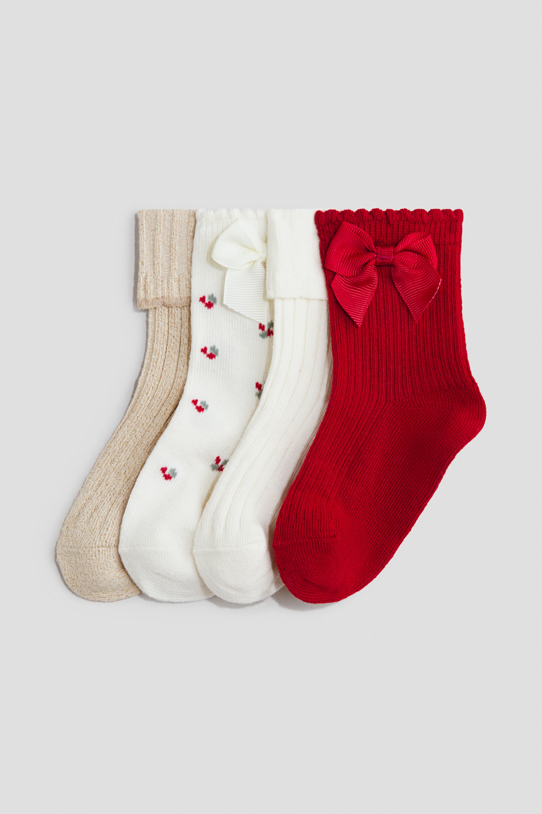 View larger image: Four socks in a soft, fine-knit cotton blend are laid side by side to show their different designs. The assortment includes a beige ribbed sock with a folded cuff, a white sock featuring a red cherry pattern and a white grosgrain bow, a cream ribbed sock with a folded cuff, and a red ribbed sock featuring a matching red grosgrain bow below a scalloped top edge.