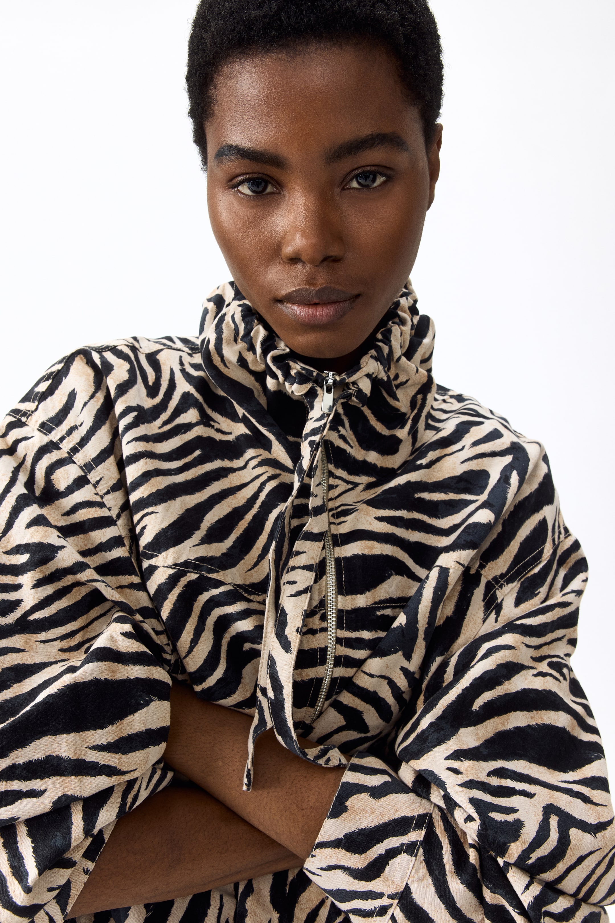 Vis større bilde: En jakke med sebramønster har en høy, rynket krage med snordetaljer og en delvis åpen sølvfarget glidelås. De voluminøse lange ermene faller elegant, noe som fremhever den avslappede passformen.