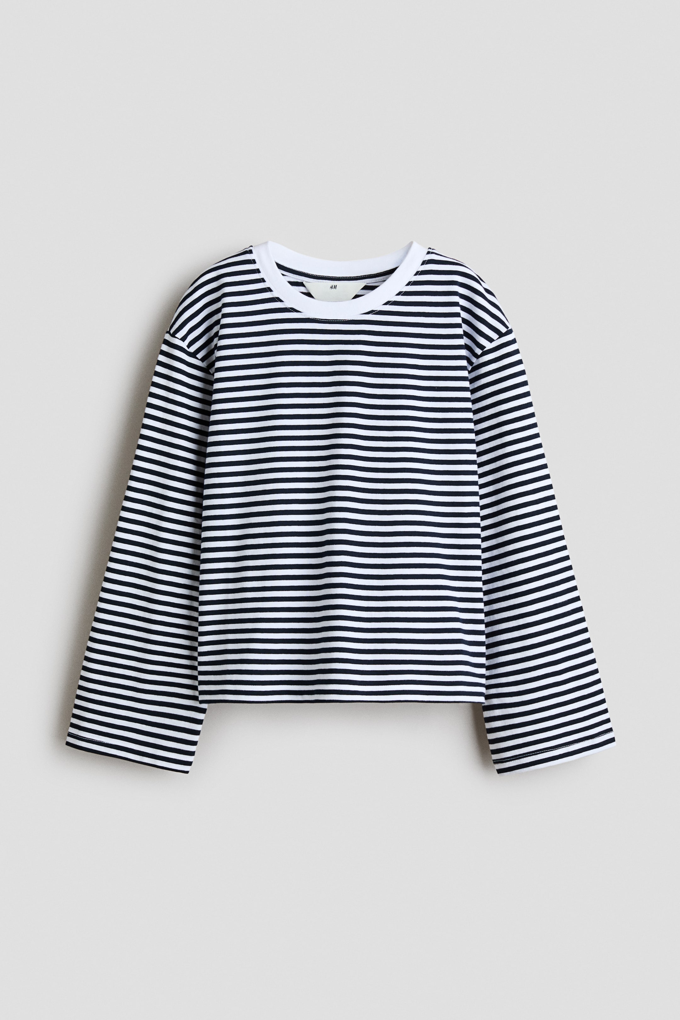View larger image: A long-sleeved t-shirt is shown from the front, featuring horizontal black and white stripes and a solid white crew neck. The garment has a relaxed fit with dropped shoulders and wide, straight sleeves.