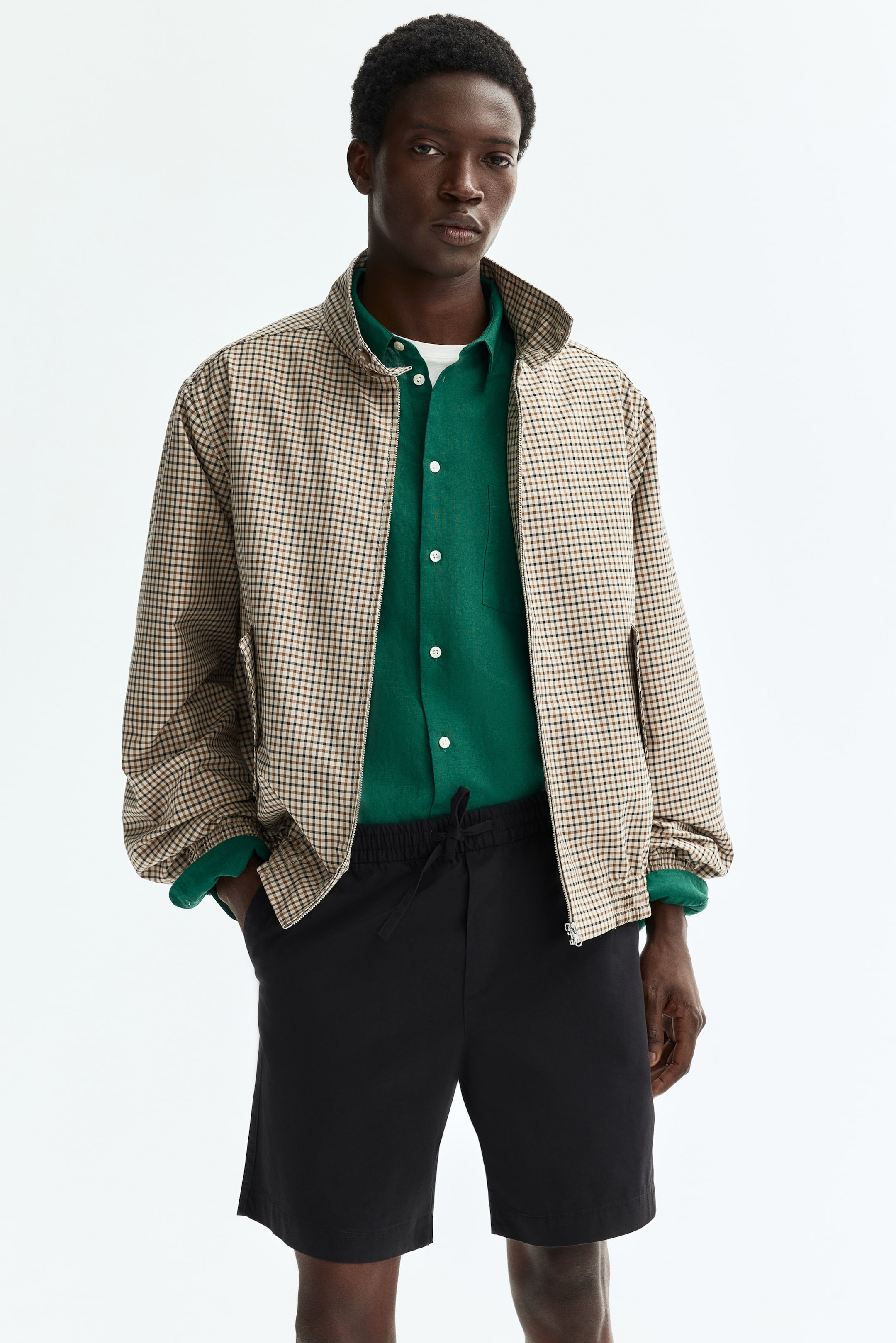 View larger image: A brown and black plaid bomber jacket features a stand-up collar, a full-zip front, side slit pockets, long sleeves with gathered cuffs, and an elastic hem. It is shown open, layered over a green long-sleeve shirt.