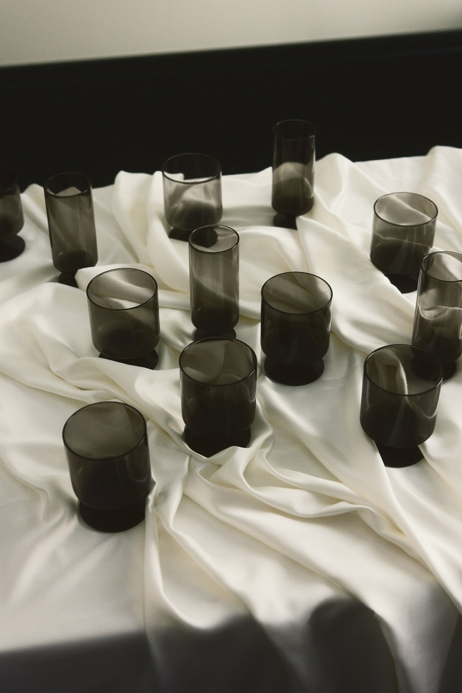 Quatre gobelets Ã  pied en verre soufflÃ© Ã  la bouche, de couleur gris fumÃ©, sont disposÃ©s en rang horizontal vus de face, mettant en valeur leur design cylindrique Ã  parois droites, leurs pieds courts et Ã©pais, ainsi que leurs bases circulaires plates. - 1