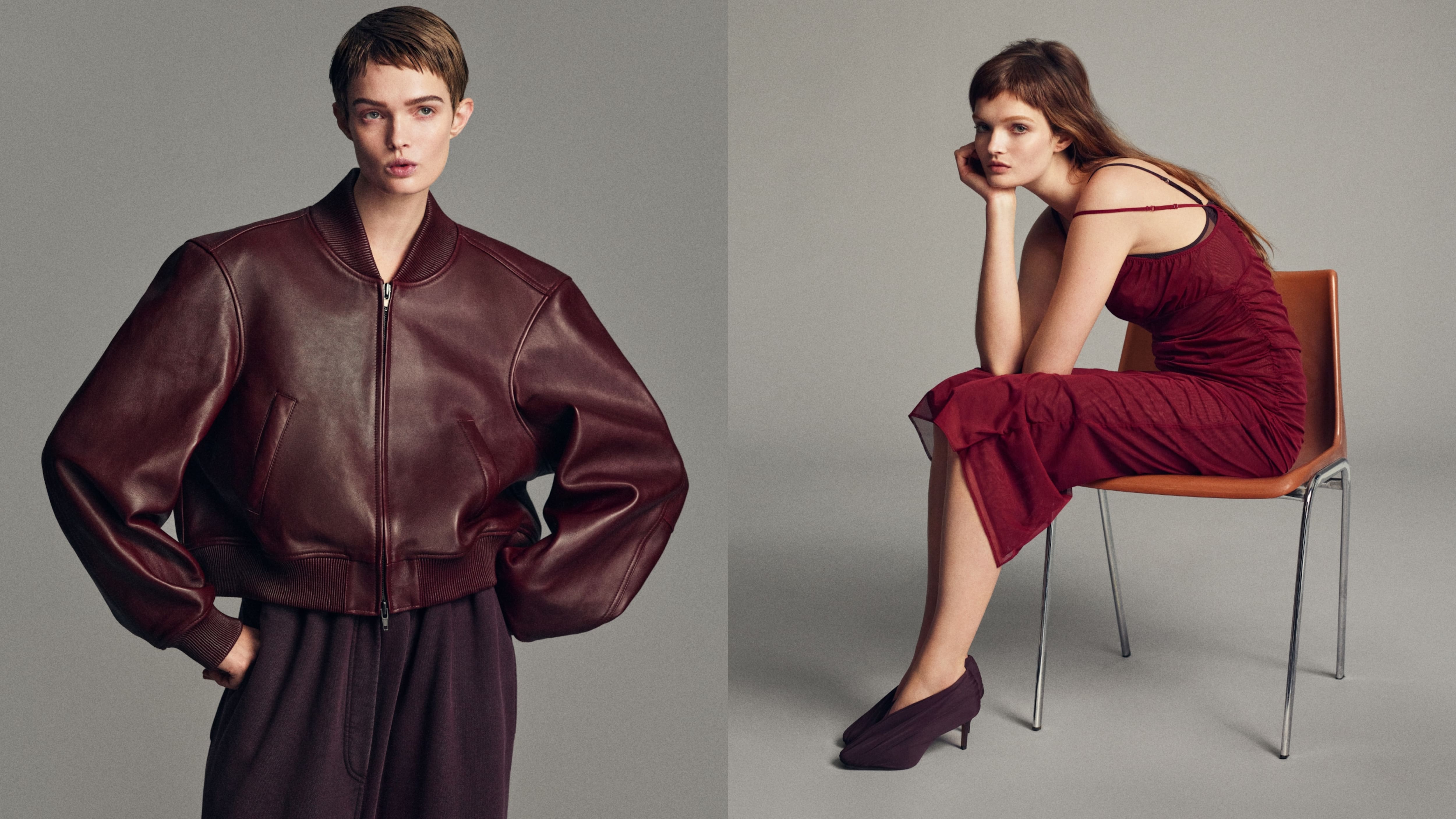 Modella che indossa una giacca bomber in pelle bordeaux con maniche scultoree, abbinata a pantaloni a gamba larga; accanto, una modella seduta in un abito rosso scuro asimmetrico con spallina cut-out, abbinato a tacchi minimalisti su uno sfondo neutro in studio.
